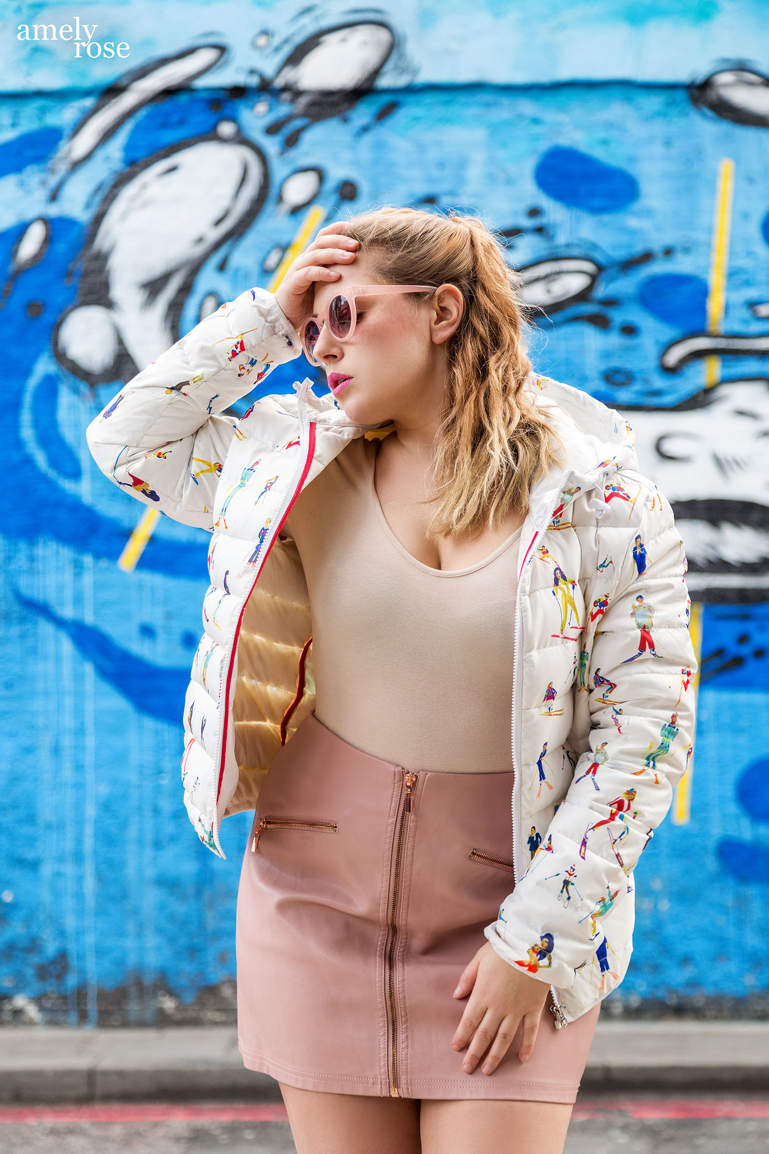 Amely Rose in einer Designer Winterjacke vor einem blauen Graffiti in London.